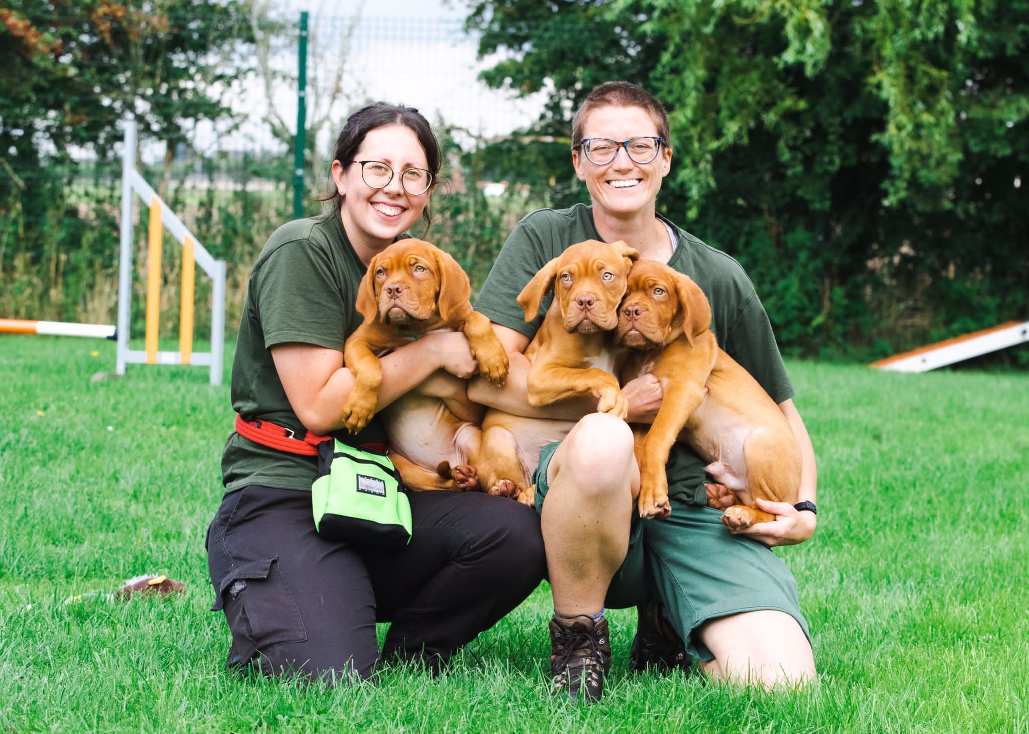 Two females in green clothing holding three Dog de Bordeaux puppies
