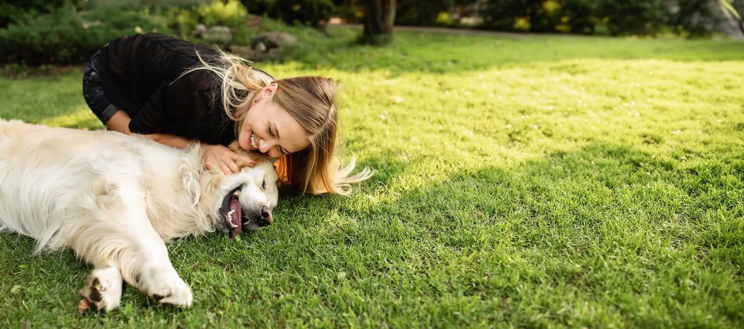 Young lady with long blonde hair kneeling on grass with golden retriever.