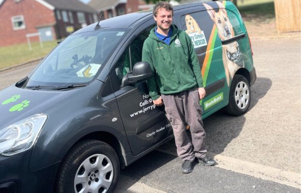 Young man wearing a Jerry Green Dog Rescue Volunteer jumper. He is standing in front of the charity van which is wrapped with images of rescue dogs