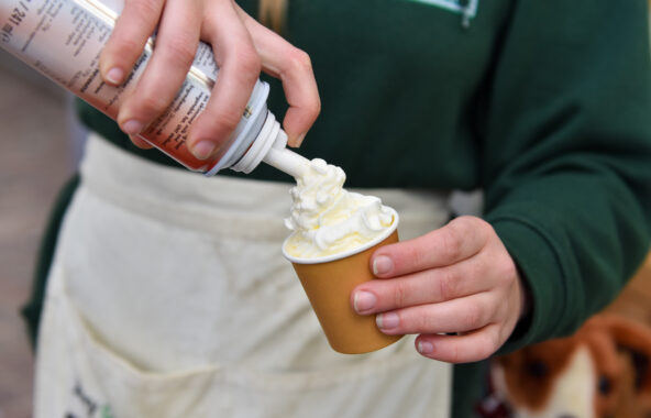Close up of a persons hands spray squirty cream into a small paper cup for a dog puppaccino