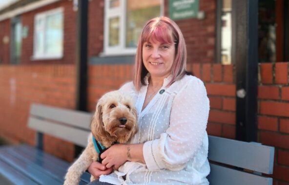 Woman wearing a white shirt, sitting on a bench, holding a cream cockapoo.