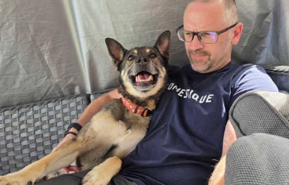 A man is sat on a sof, cuddled up next to a German Shepherd crossbredd dog.