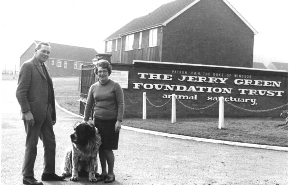 Black and white photograph of Jerry Green Dog Rescue Broughton in 1961 with two people stood in front of the opening sign with a large breed dog