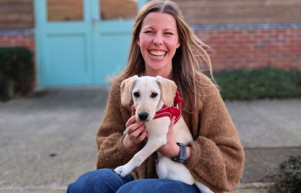 Smiling woman with long brown hair holding a cream coloured dog with floppy ears.