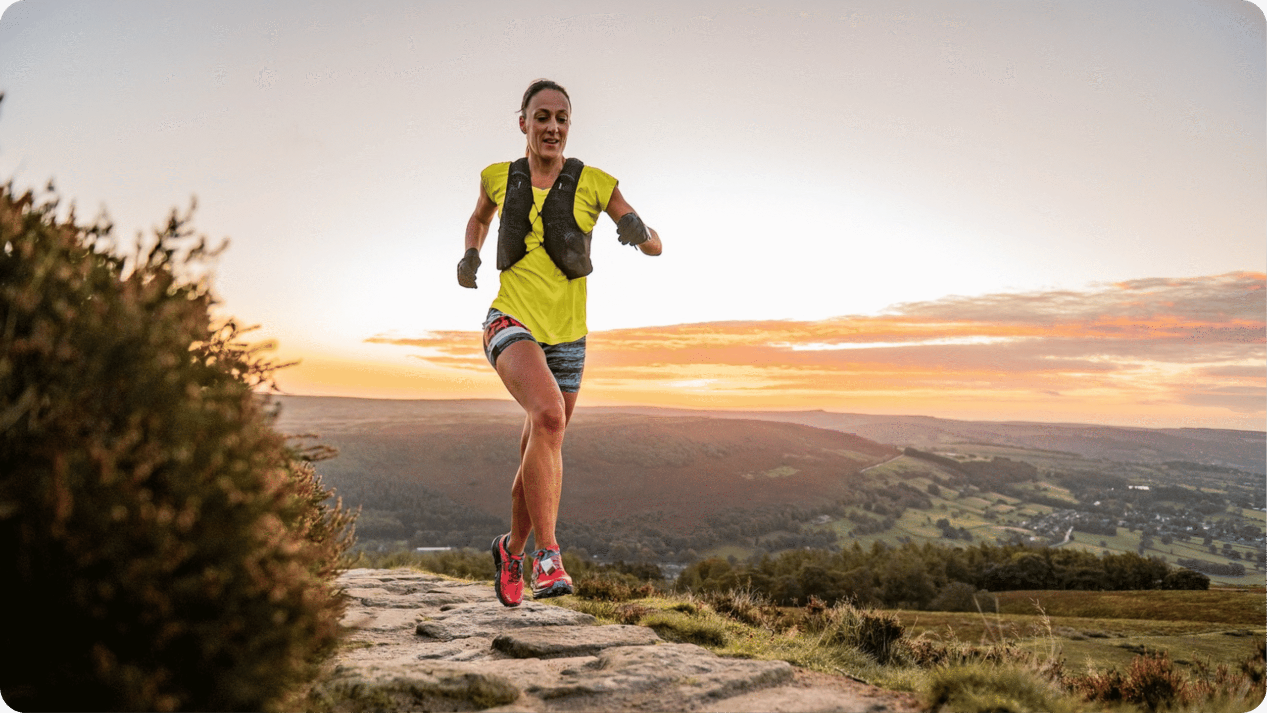 Runner in yellow t-shirt and shorts on stony path high on a hillside.