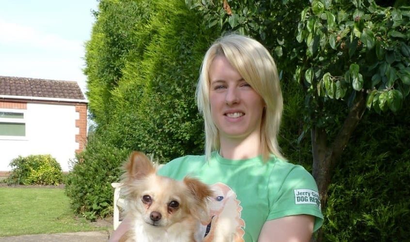 Young woman with blonde hair holding a small tan and white dog.