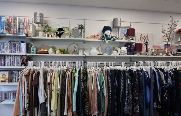 Shelves of various ornaments and hanging rail of assorted garments on white hangers.