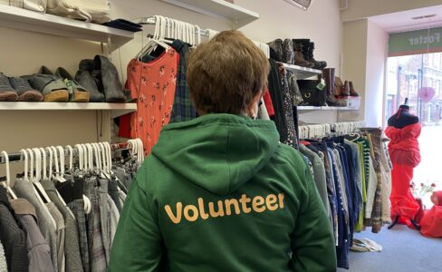 A person stood in a shop with their back to the camera wearing a green hoodie which says volunteer on the back in orange font.