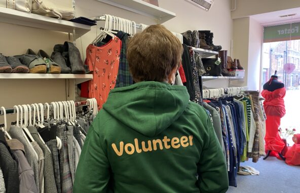 A person stood in a shop with their back to the camera wearing a green hoodie which says volunteer on the back in orange font.