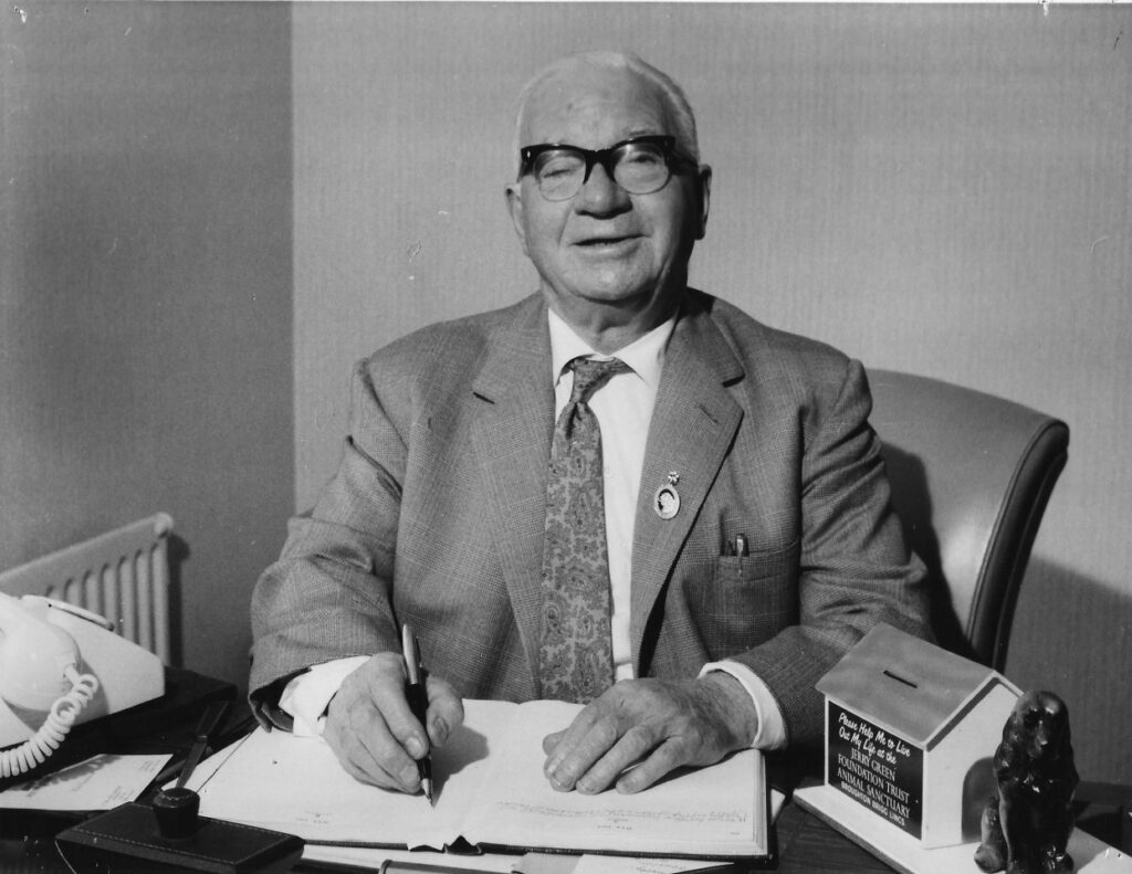 Black and white photo of older man sat at a desk signing some paperwork