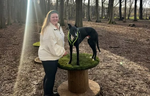 Young woman with black lurcher that's standing on a wooden drum.