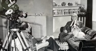 Black and white photo of a man in the 1960s sat on a sofa with a Cocker Spaniel being interviewed by a man sat opposite with a film reel camera behind him