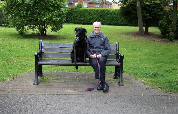 Person with black dog sitting on a park bench.
