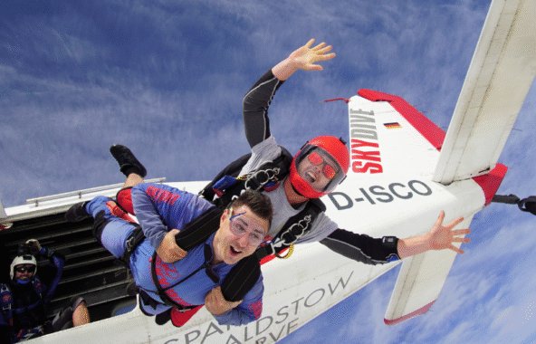 Tandem skydivers jumping out of red and white aircraft.