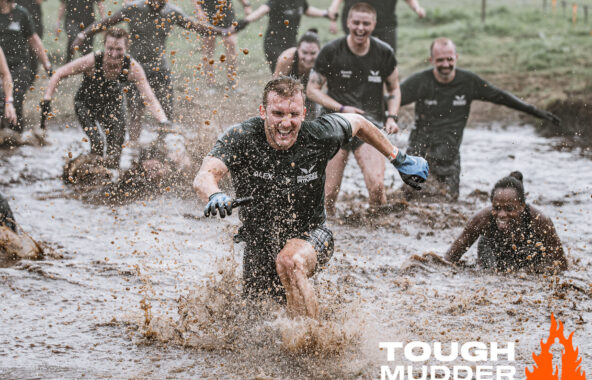 Competitors dressed in black running through muddy water for the Tough Mudder challenge.