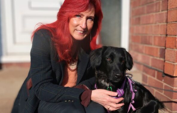 Woman with red hair kneeling with a black labrador.