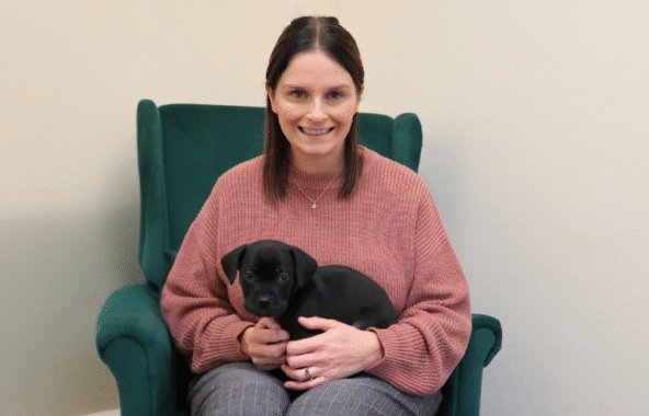 Sarah Wilson, trustee of Jerry Green Dog Rescue, sitting in a blue chair with a black puppy on her lap.