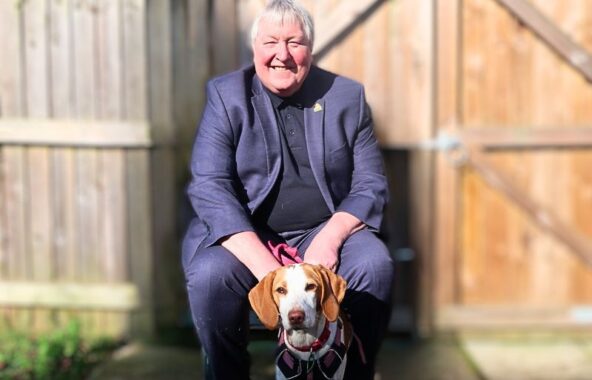 Man with grey hair sitting in front of a fence with a tan and white dog.