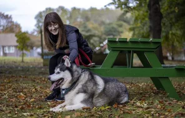 Person sitting at a picnic table petting a husky.