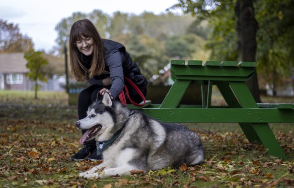 Person sitting at a picnic table petting a husky.