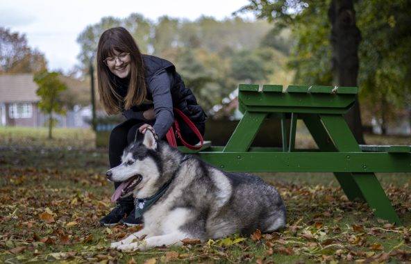 Person sitting at a picnic table petting a husky.
