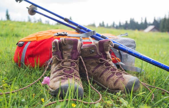 A pair of walking boots with a backpack and walking sticks resting on top in a field.