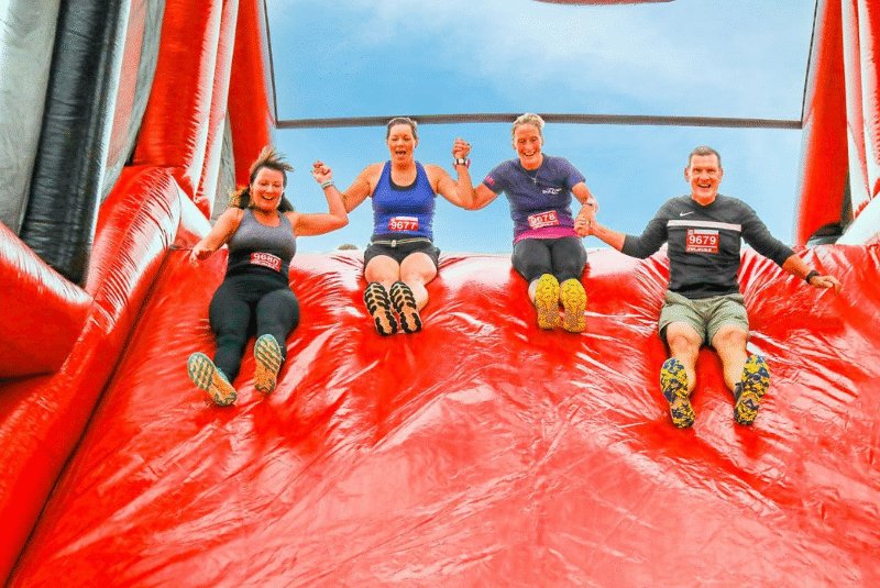 Four people sat going down a large red inflatable slide