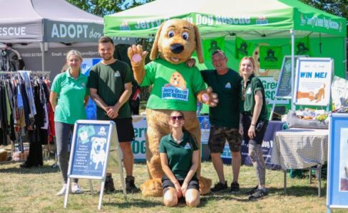 Several people stood in front of a green stall with a large dog mascot in the middle which has a Jerry Green Dog Rescue logo on the front
